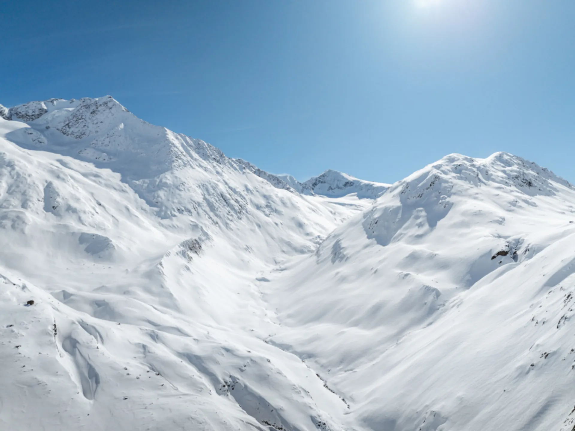 Verschneite Berggipfel und ein schneebedecktes Tal unter blauem Himmel
