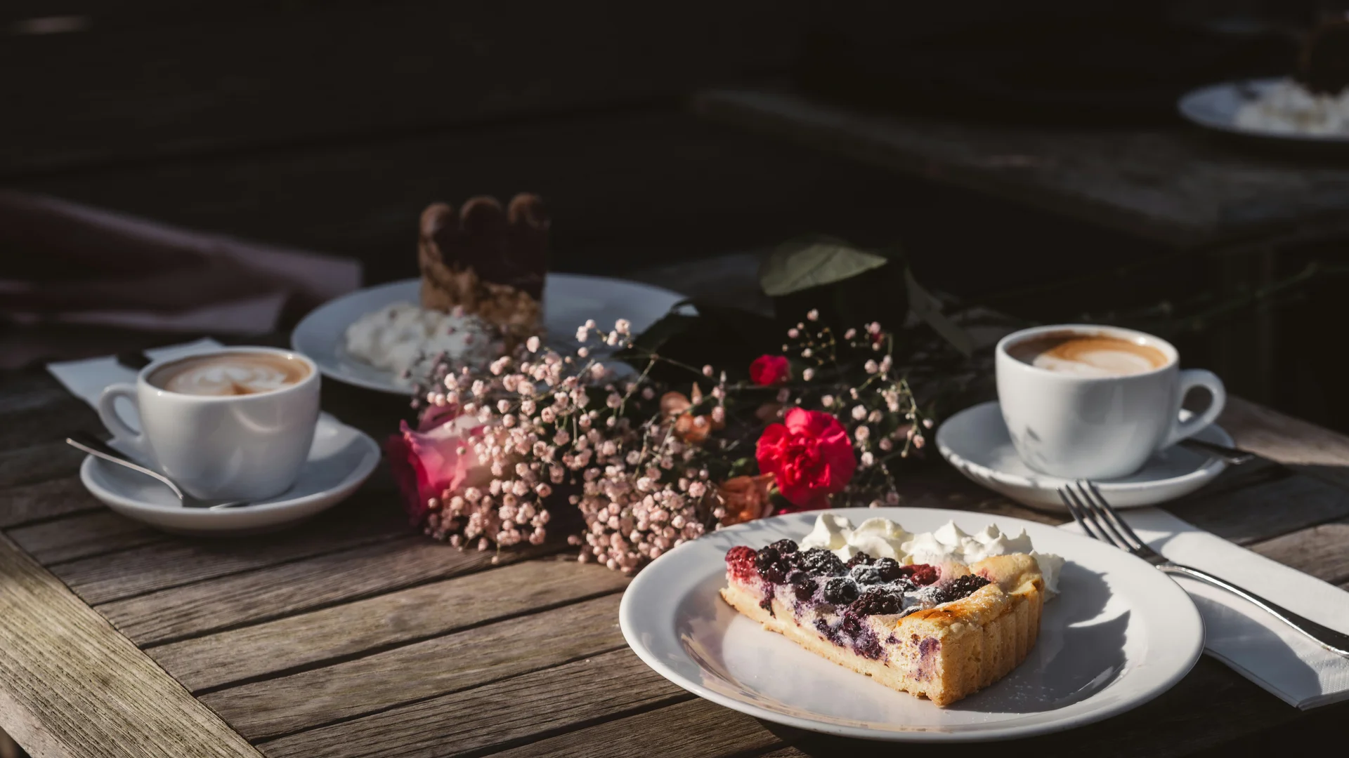 Coffee, berry cake and flowers on a wooden table