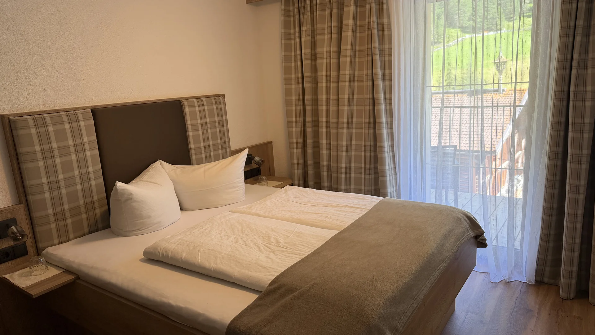 Gemütliches Doppelbett mit kariertem Kopfteil und Balkonfenster