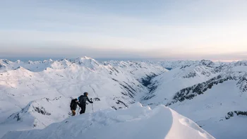 Zwei Wanderer besteigen schneebedeckten Berg mit Alpenpanorama bei Sonnenuntergang