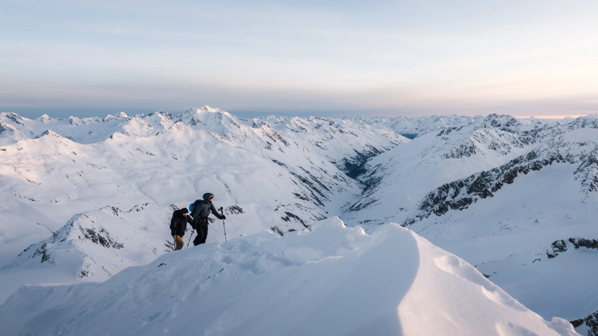 Snowy adventures on winter holidays in the Alps Zwei Wanderer besteigen schneebedeckten Berg mit Alpenpanorama bei Sonnenuntergang