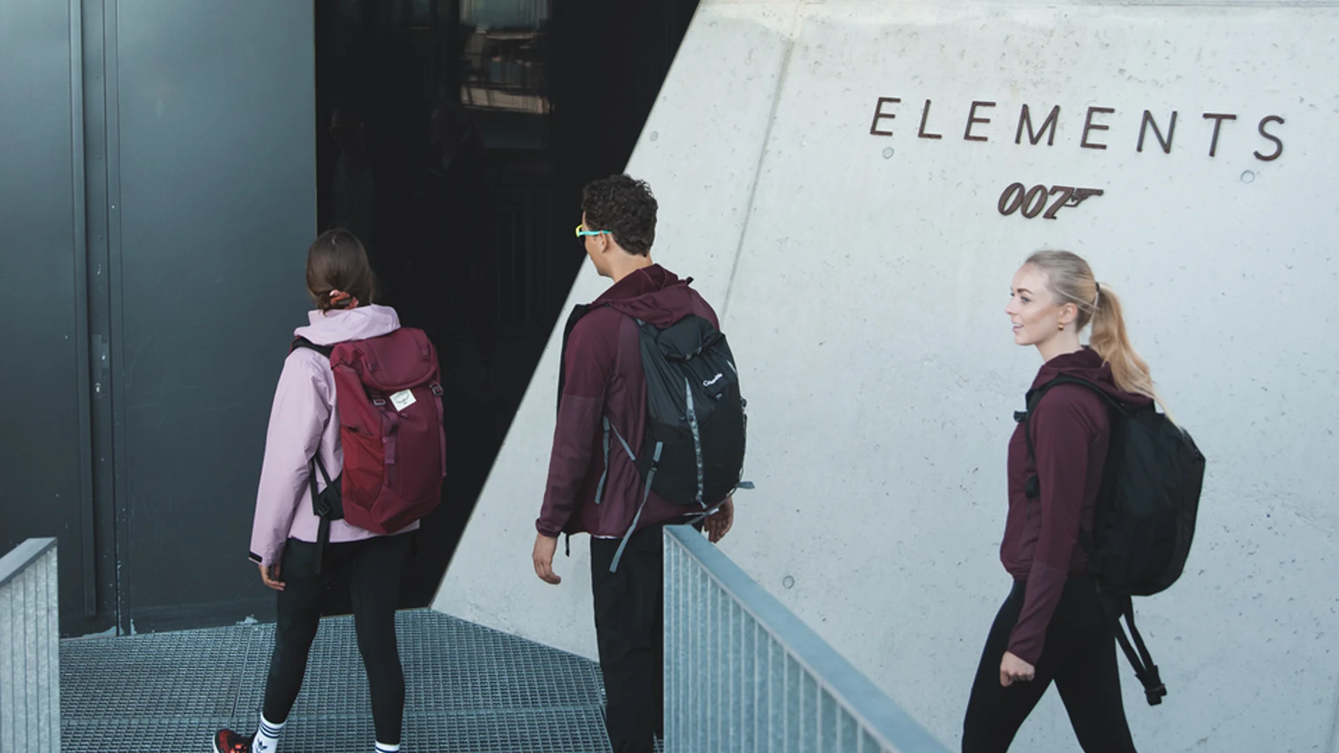Drei Wanderer mit Rucksäcken betreten das Gebäude Elements 007