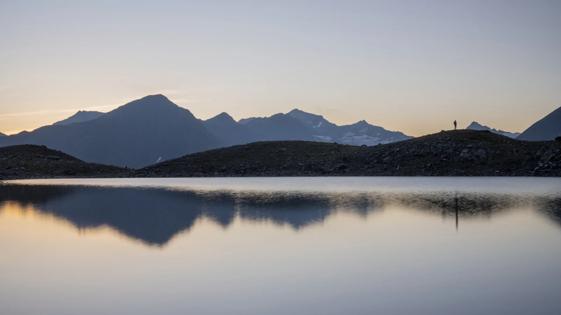 Berglandschaft mit See und Person auf Hügel bei Sonnenuntergang