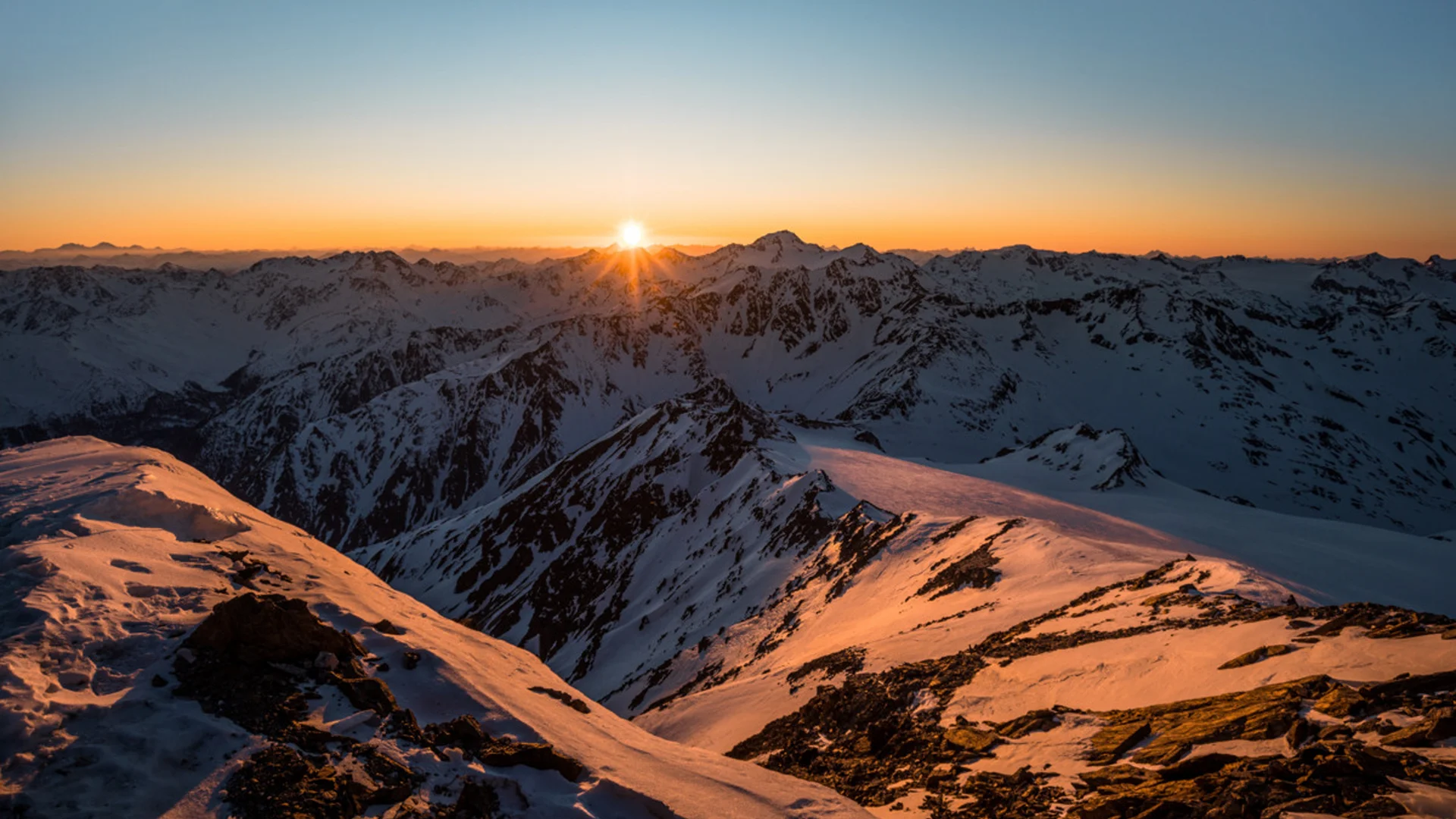 Sonnenaufgang über schneebedeckten Bergen mit orangefarbenem Himmel