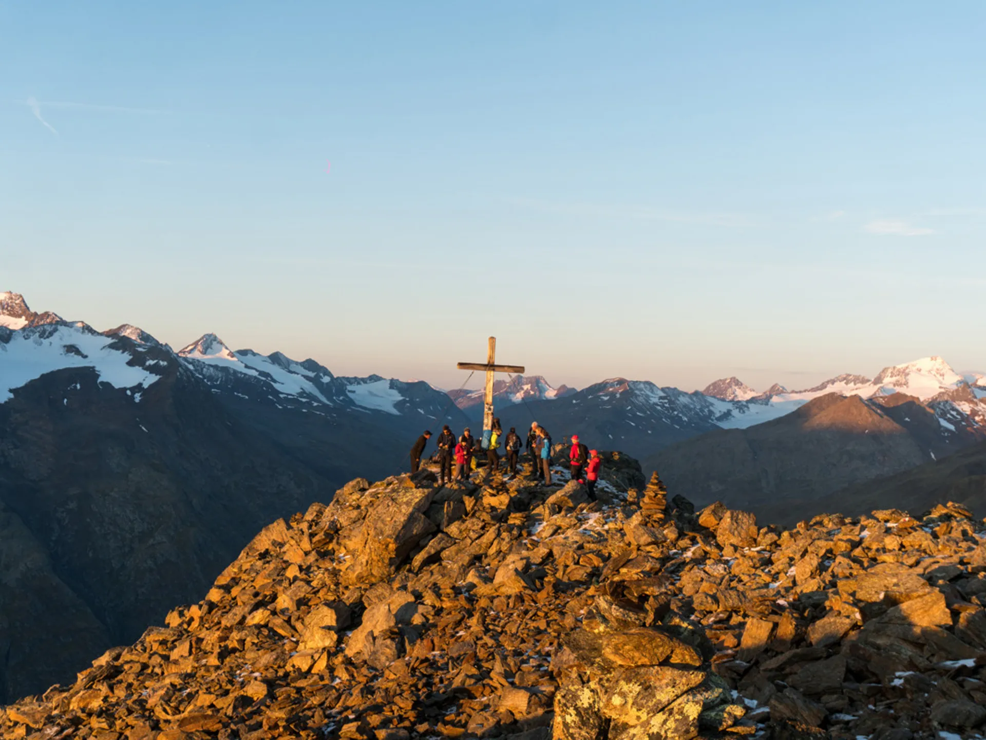 Group of hikers on rocky mountain summit with cross at sunset