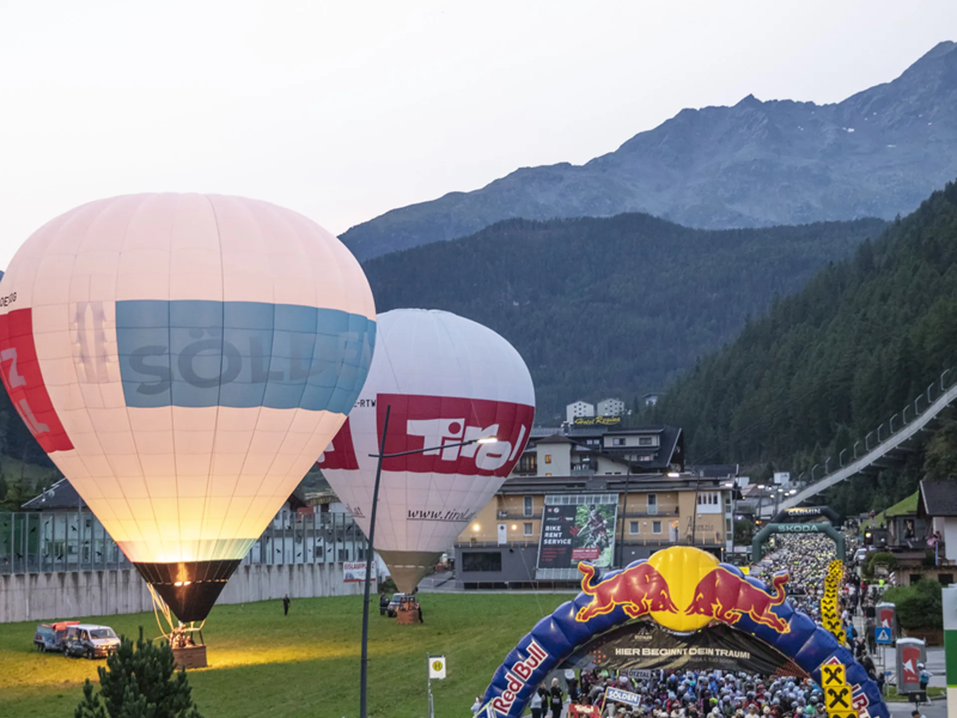 Crowd beneath a Red Bull arch with hot-air balloons and mountain scenery