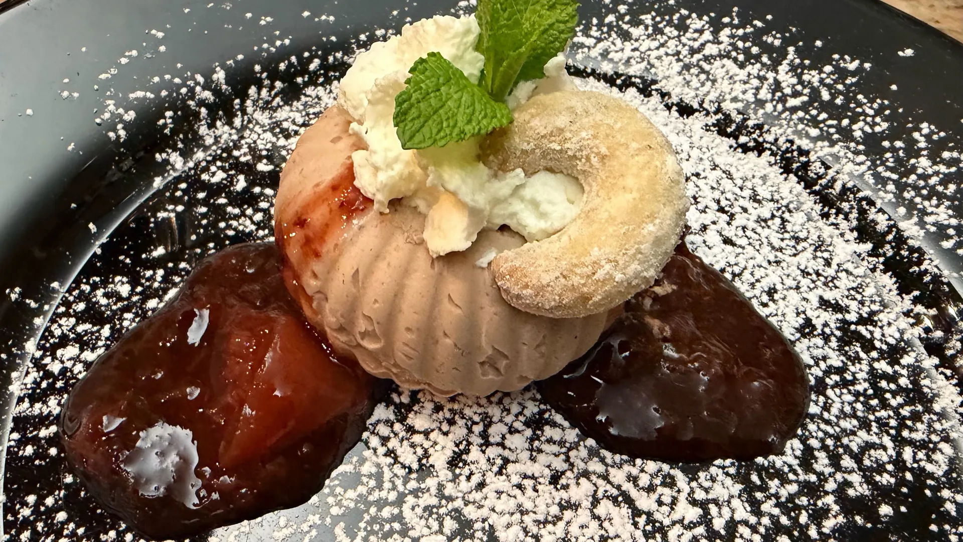 Gasthof Weisskugel: Bilder, die Sehnsucht wecken Dessert mit Eis, Schlagsahne, Minze, Puderzucker und Fruchtsoßen auf schwarzem Teller