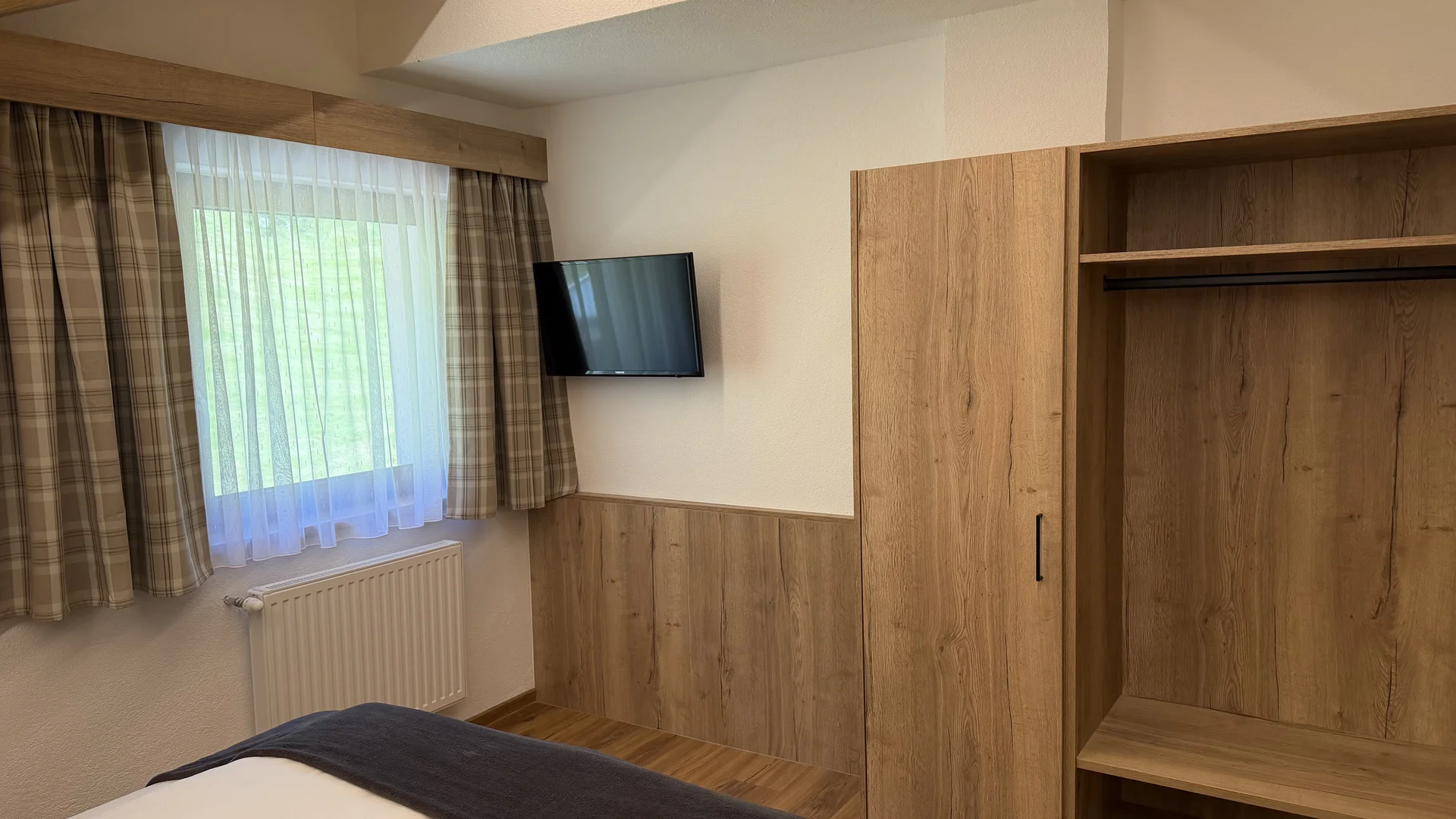 Bedroom with bed, television, window and open wooden wardrobe