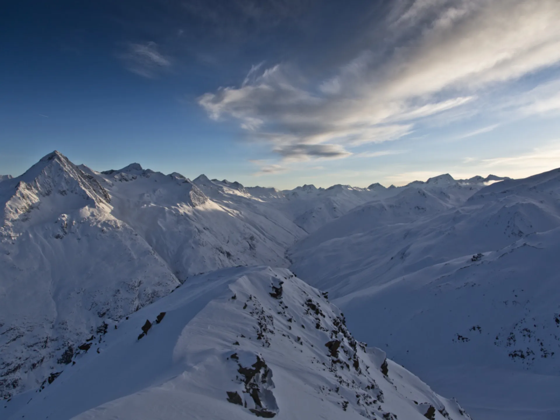 Verschneite Berggipfel und ein schmaler Grat unter einem bewölkten Himmel