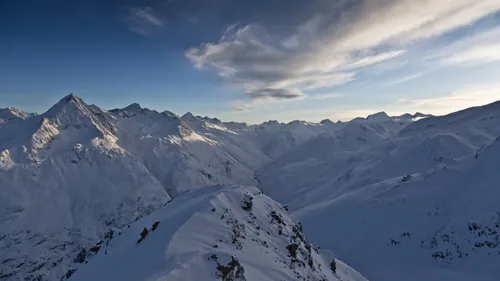 Verschneite Berggipfel und ein schmaler Grat unter einem bewölkten Himmel