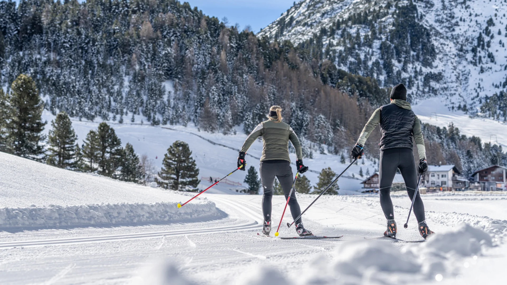 Zwei Personen beim Langlaufen auf verschneiter Loipe vor Bergkulisse