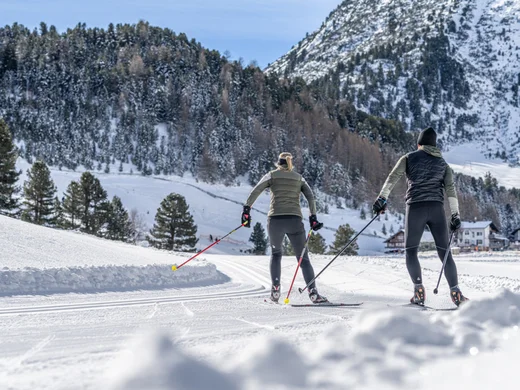 Snowy adventures on winter holidays in the Alps Zwei Personen beim Langlaufen auf verschneiter Loipe vor Bergkulisse