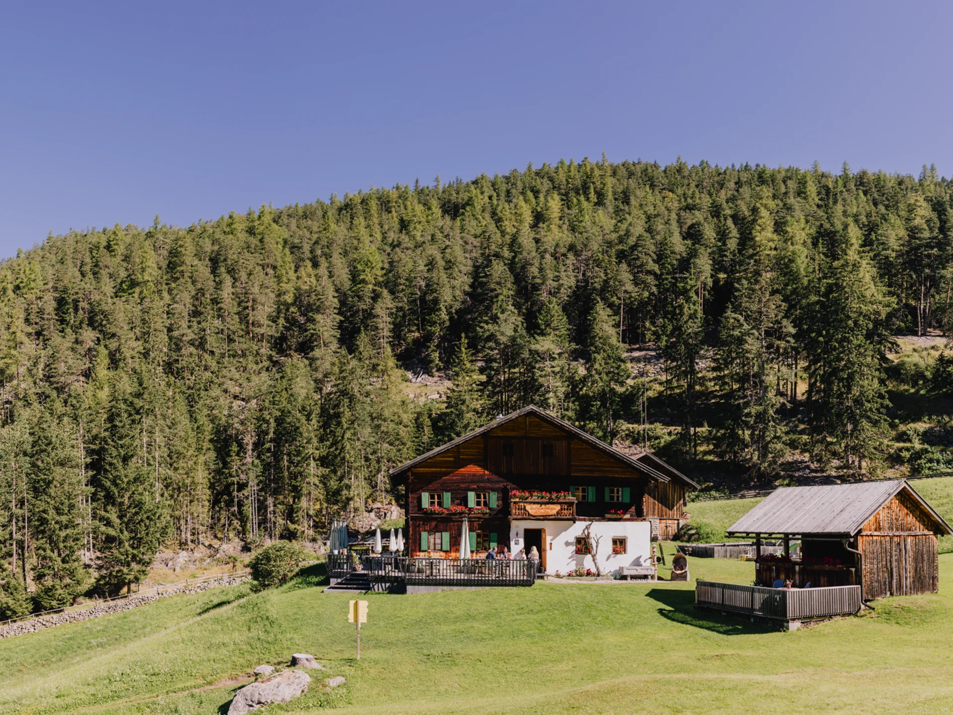 Weisskugel: your accommodation in Tyrol Altes Bauernhaus mit Terrasse vor bewaldetem Hügel unter klarem Himmel