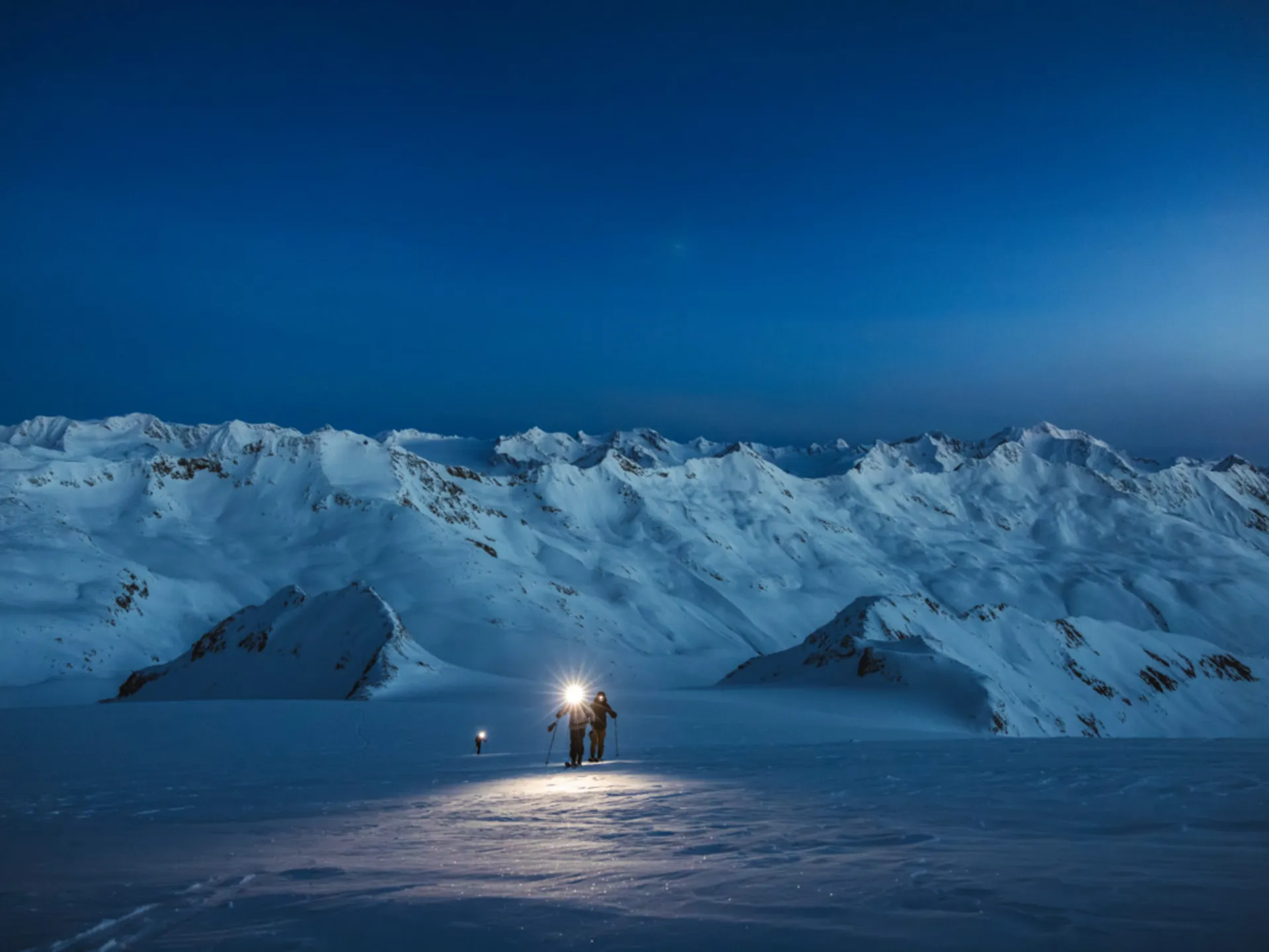 Menschen mit Stirnlampen wandern nachts durch eine verschneite Berglandschaft