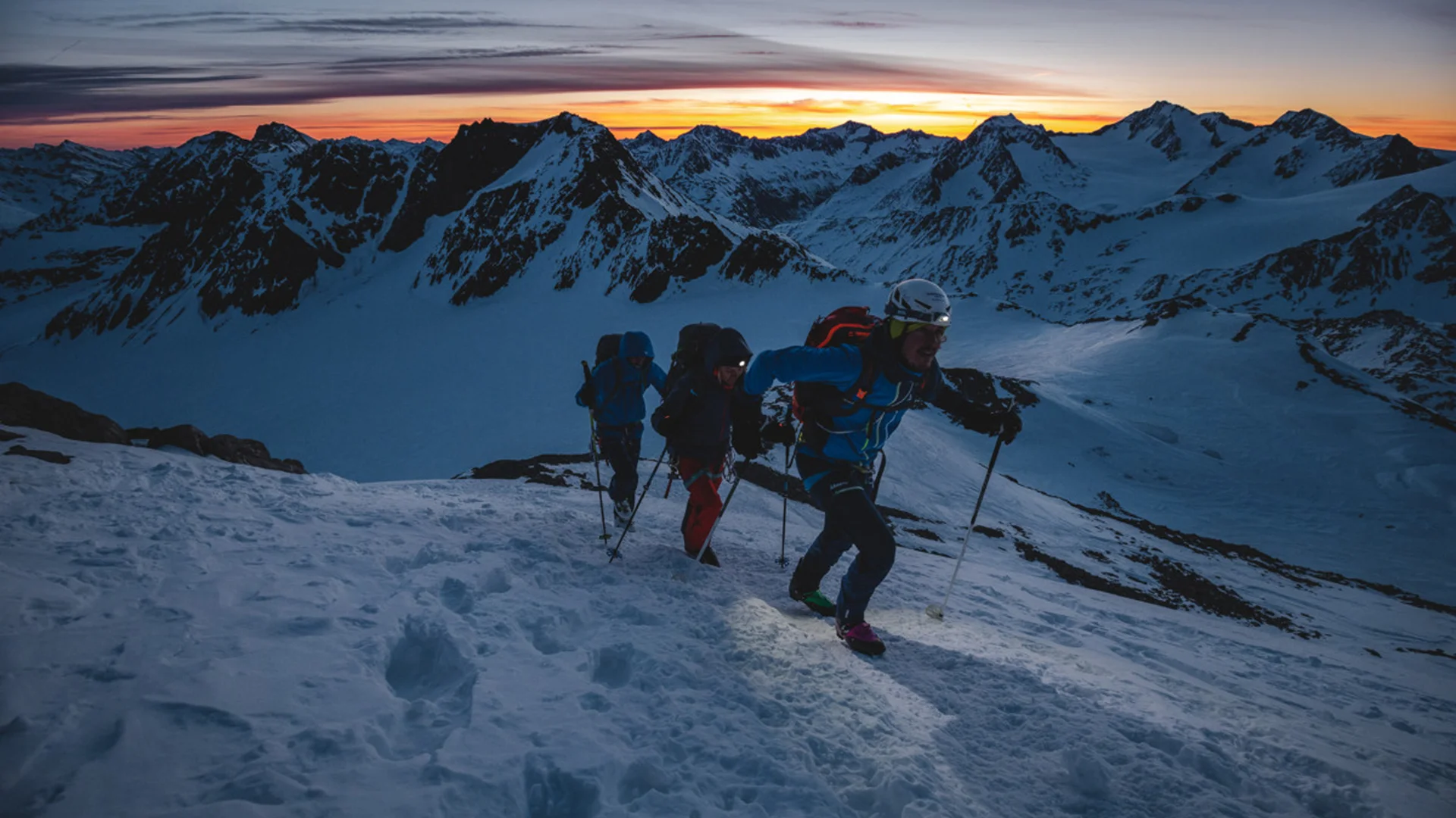 Drei Bergsteiger steigen bei Sonnenaufgang durch verschneite Berge