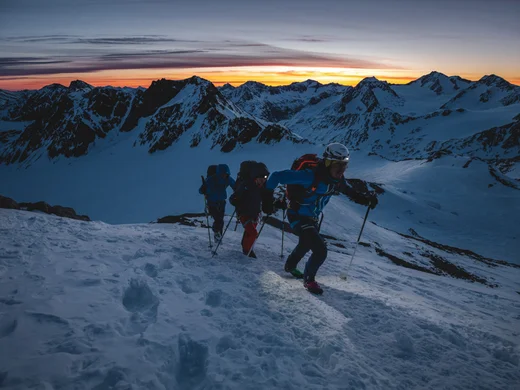 Snowy adventures on winter holidays in the Alps Drei Bergsteiger steigen bei Sonnenaufgang durch verschneite Berge