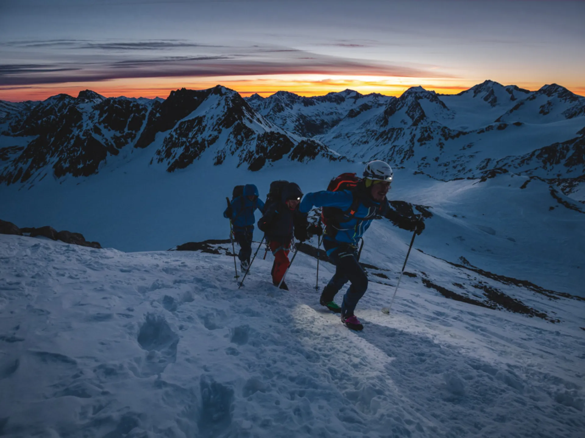 Drei Bergsteiger steigen bei Sonnenaufgang einen verschneiten Hang hinauf