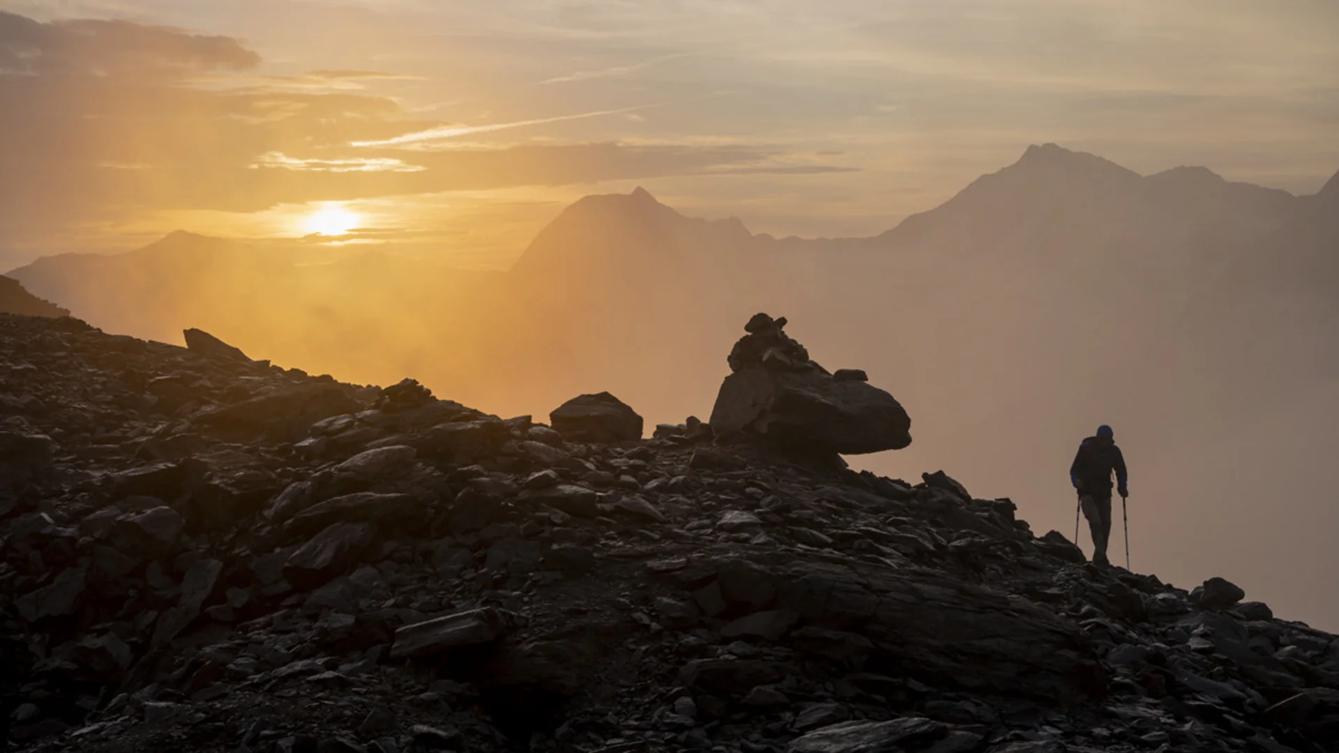 Weisskugel: your accommodation in Tyrol Wanderer auf felsigem Bergpfad bei Sonnenaufgang mit Nebel und Bergen
