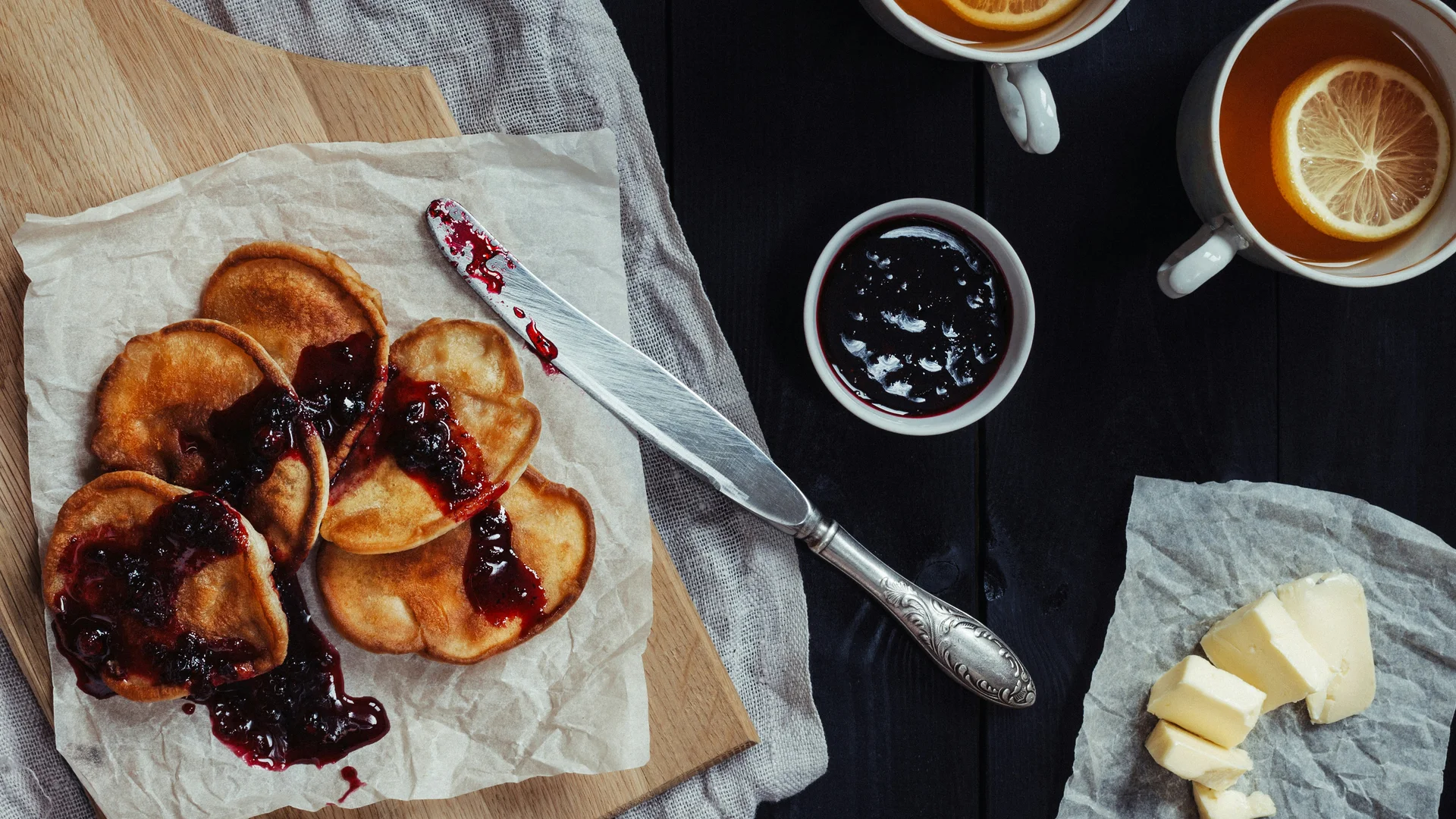 Pancakes with berry jam, tea with orange slices and butter on a table
