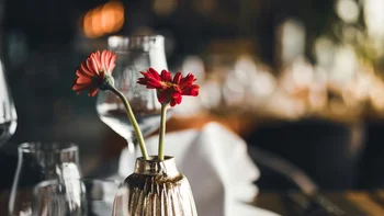 Restaurant table with vase, red flowers, glasses and folded napkin