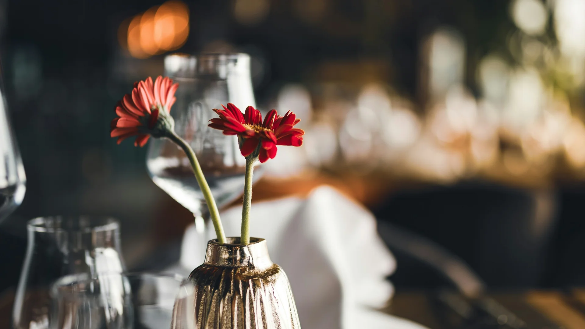 Restaurant table with vase, red flowers, glasses and folded napkin