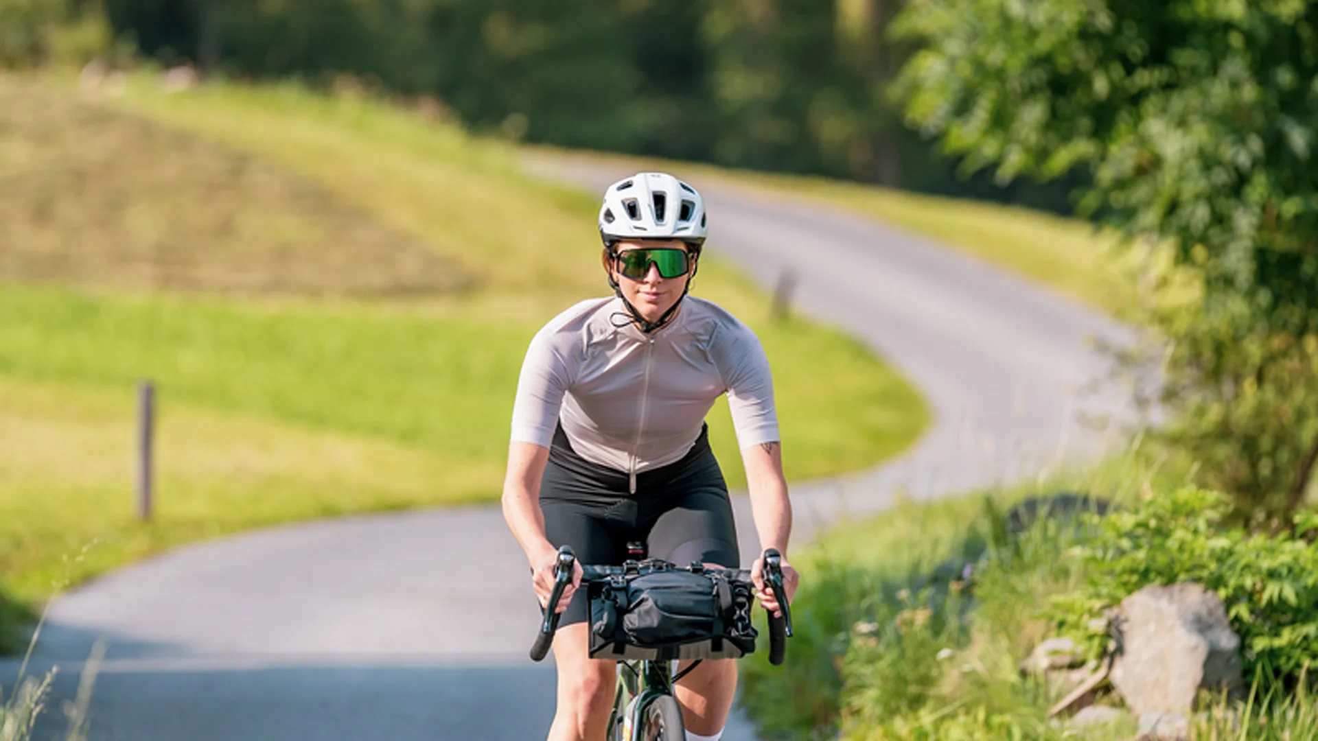 Frau fährt Fahrrad auf kurviger Landstraße umgeben von grüner Natur