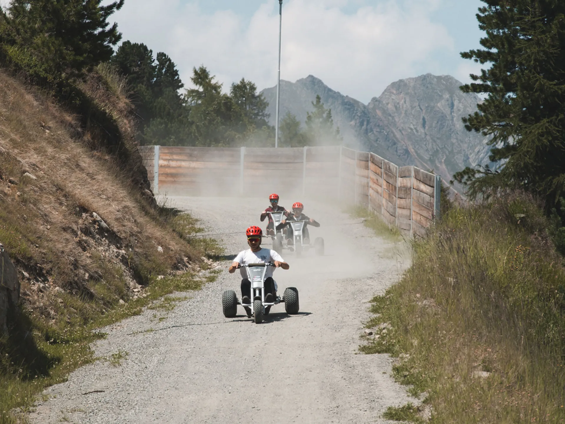 Three people ride off-road karts along a dusty mountain path