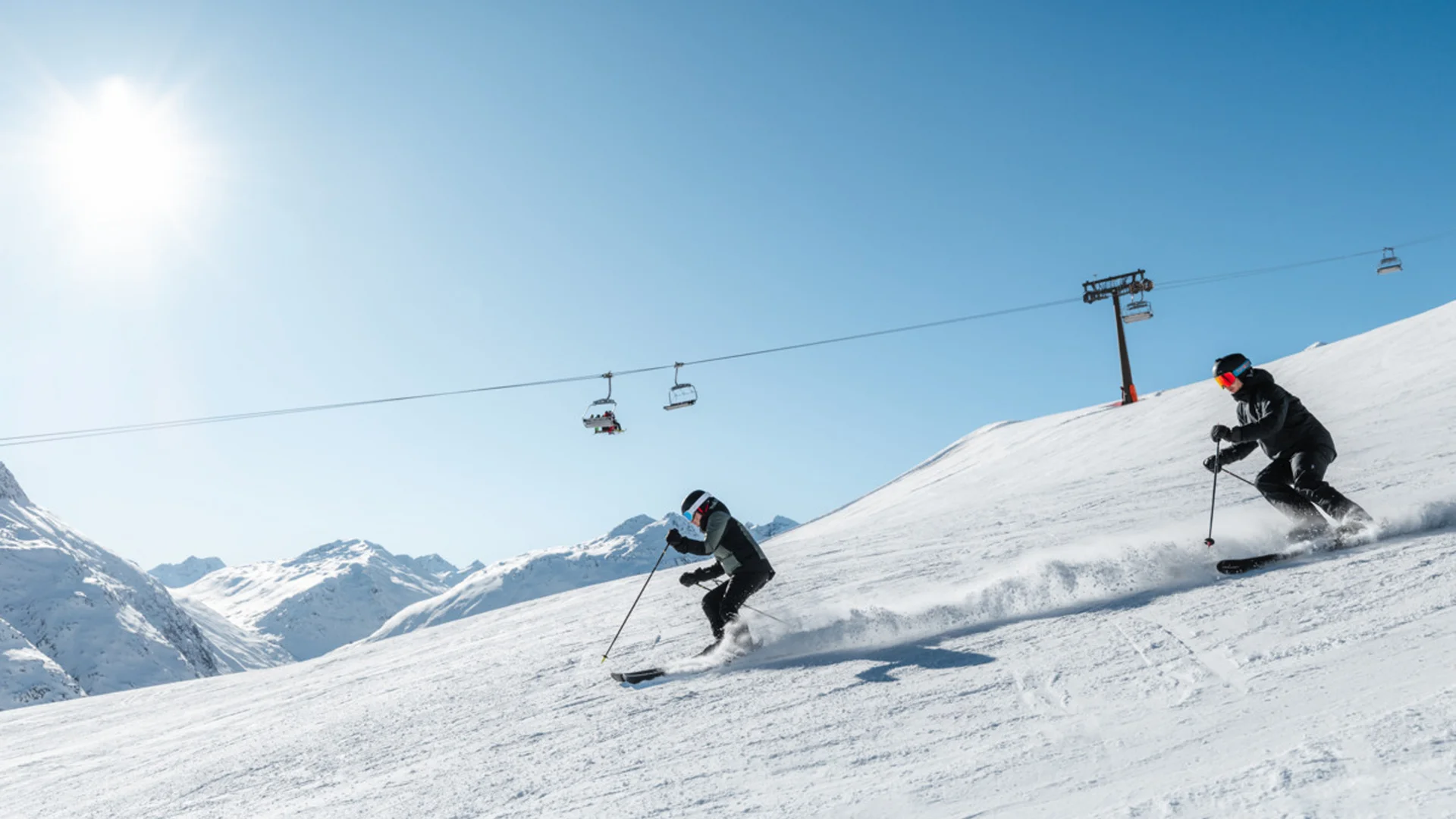 Zwei Skifahrer fahren bei sonnigem Wetter auf schneebedecktem Berghang