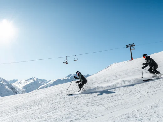 Snowy adventures on winter holidays in the Alps Zwei Skifahrer fahren bei sonnigem Wetter auf schneebedecktem Berghang