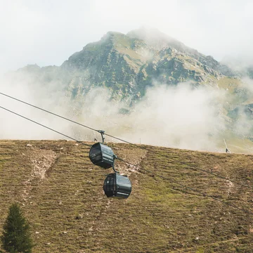 Weisskugel: your accommodation in Tyrol Zwei Gondelbahnkabinen über grasbewachsenem Berghang mit wolkigem Himmel