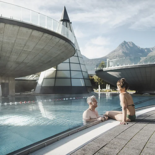 Älteres Paar entspannt am Außenpool mit moderner Architektur und Bergen im Hintergrund
