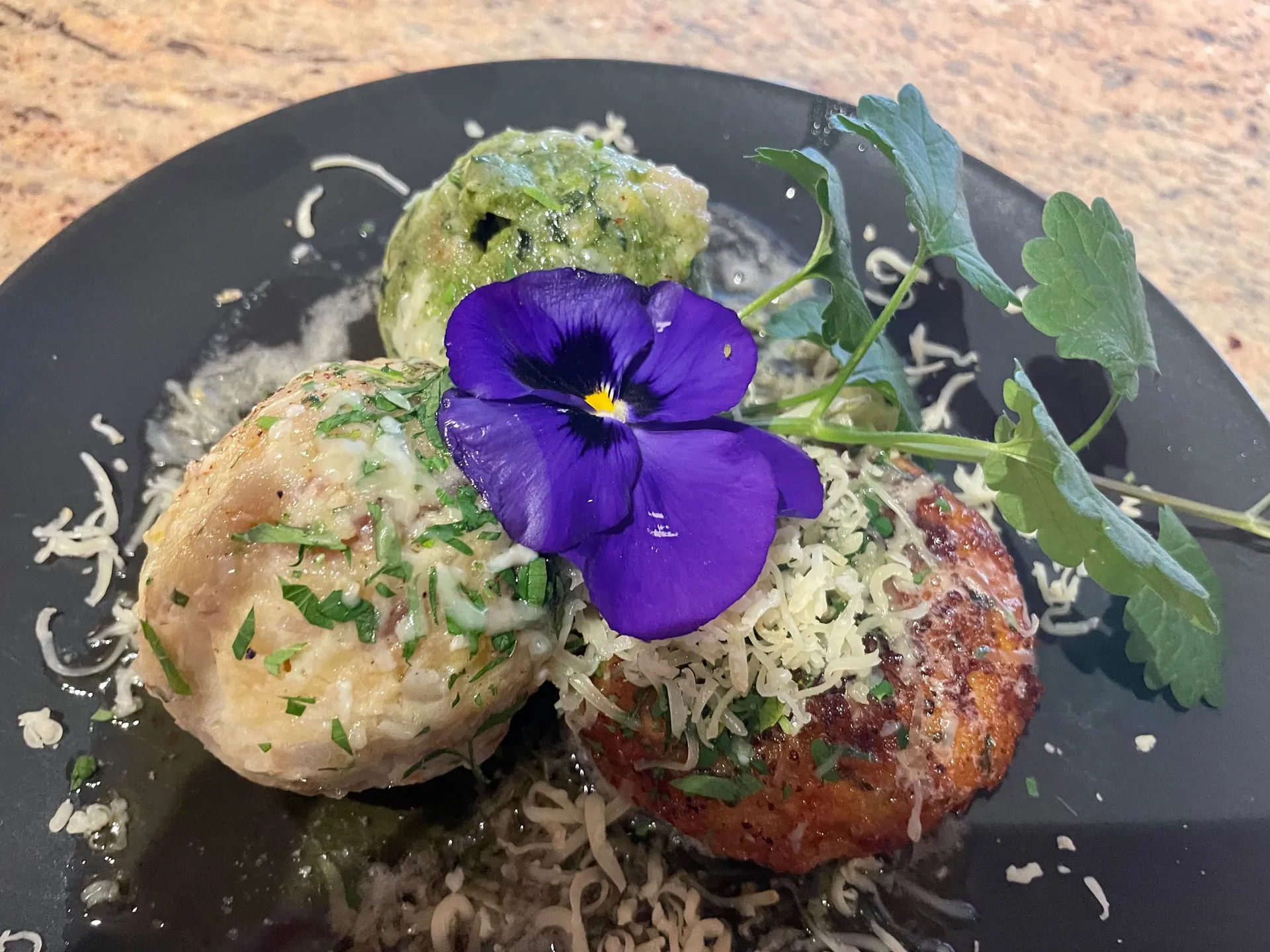 Weisskugel: your accommodation in Tyrol Two fried foods with grated cheese, herbs and a purple flower on a black plate
