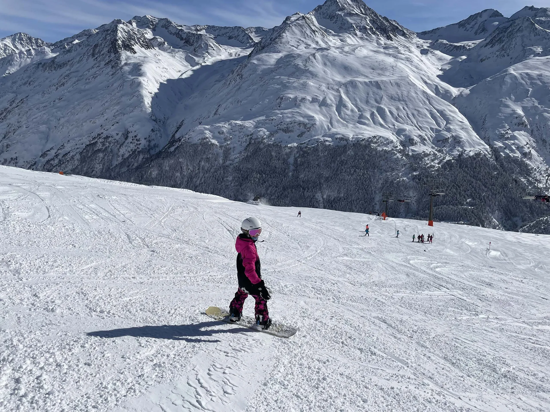 Snowboarder in pinker Jacke auf einer Piste vor schneebedeckten Bergen