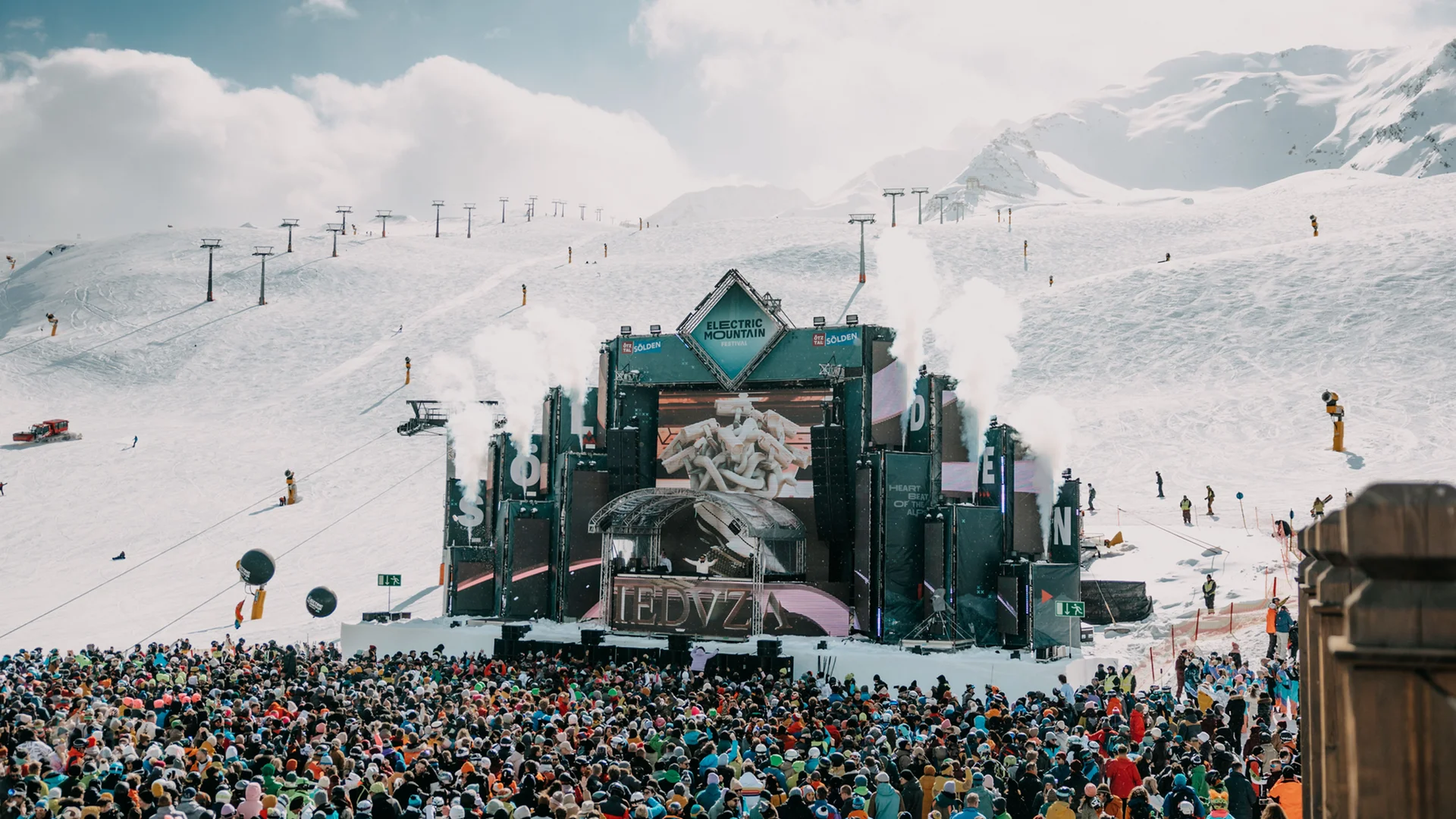 Große Menschenmenge vor Bühne bei Musikfestival in schneebedeckten Bergen
