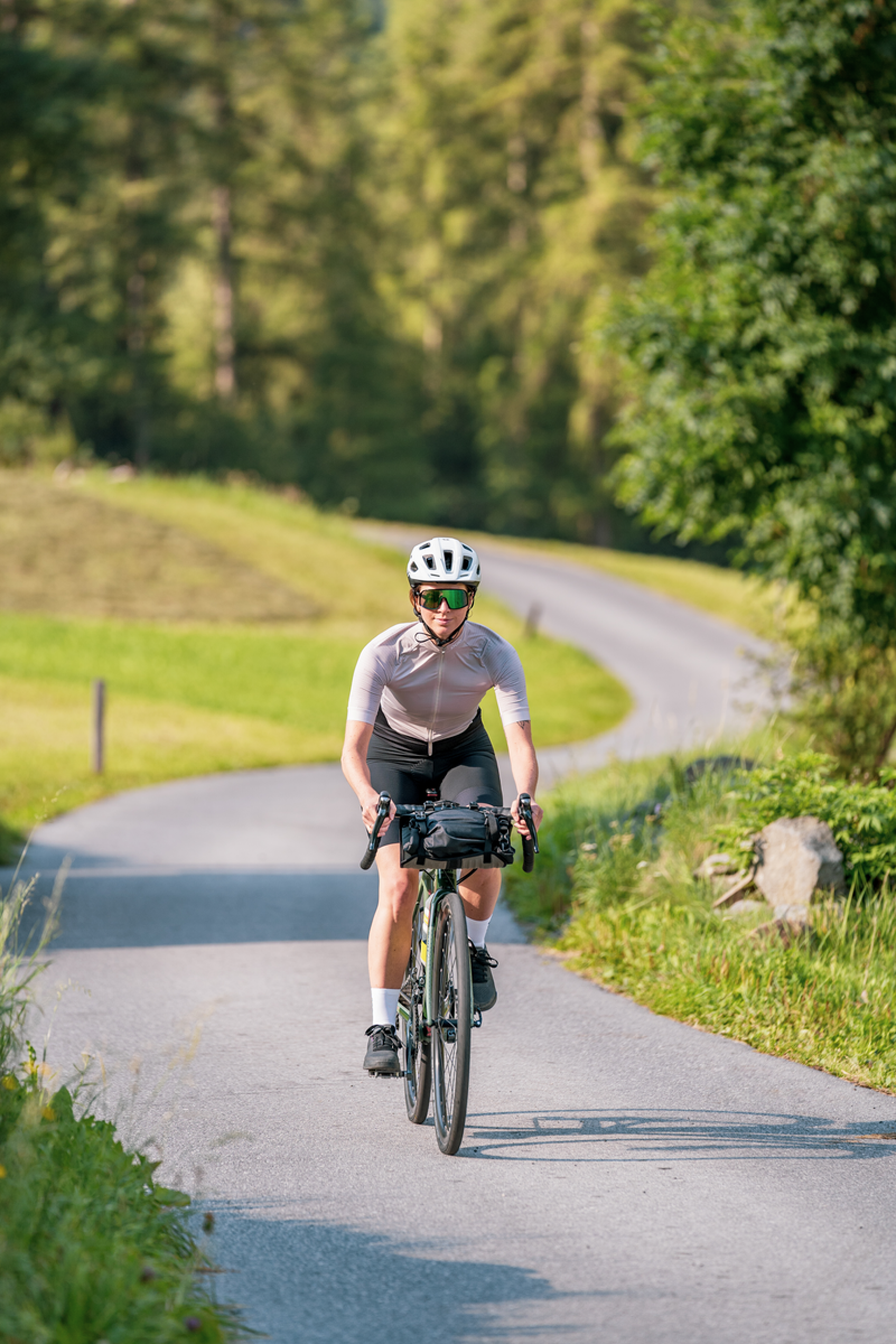 Frau fährt Fahrrad auf kurviger Landstraße umgeben von grüner Natur