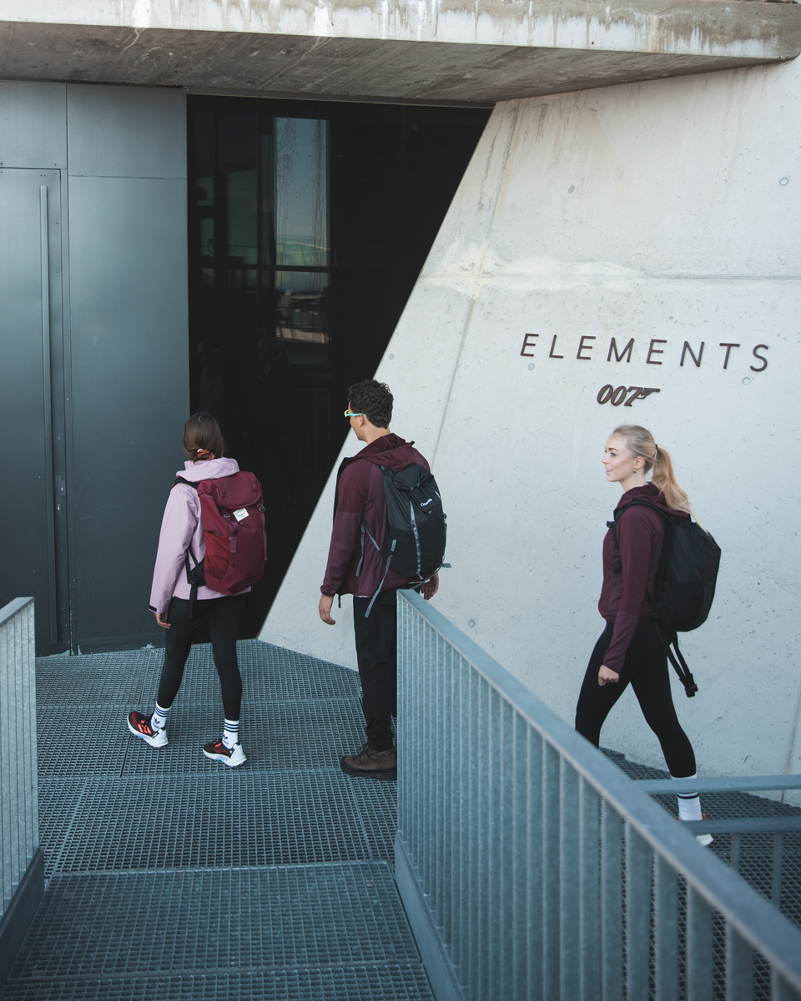 Drei Wanderer mit Rucksäcken betreten das Gebäude Elements 007