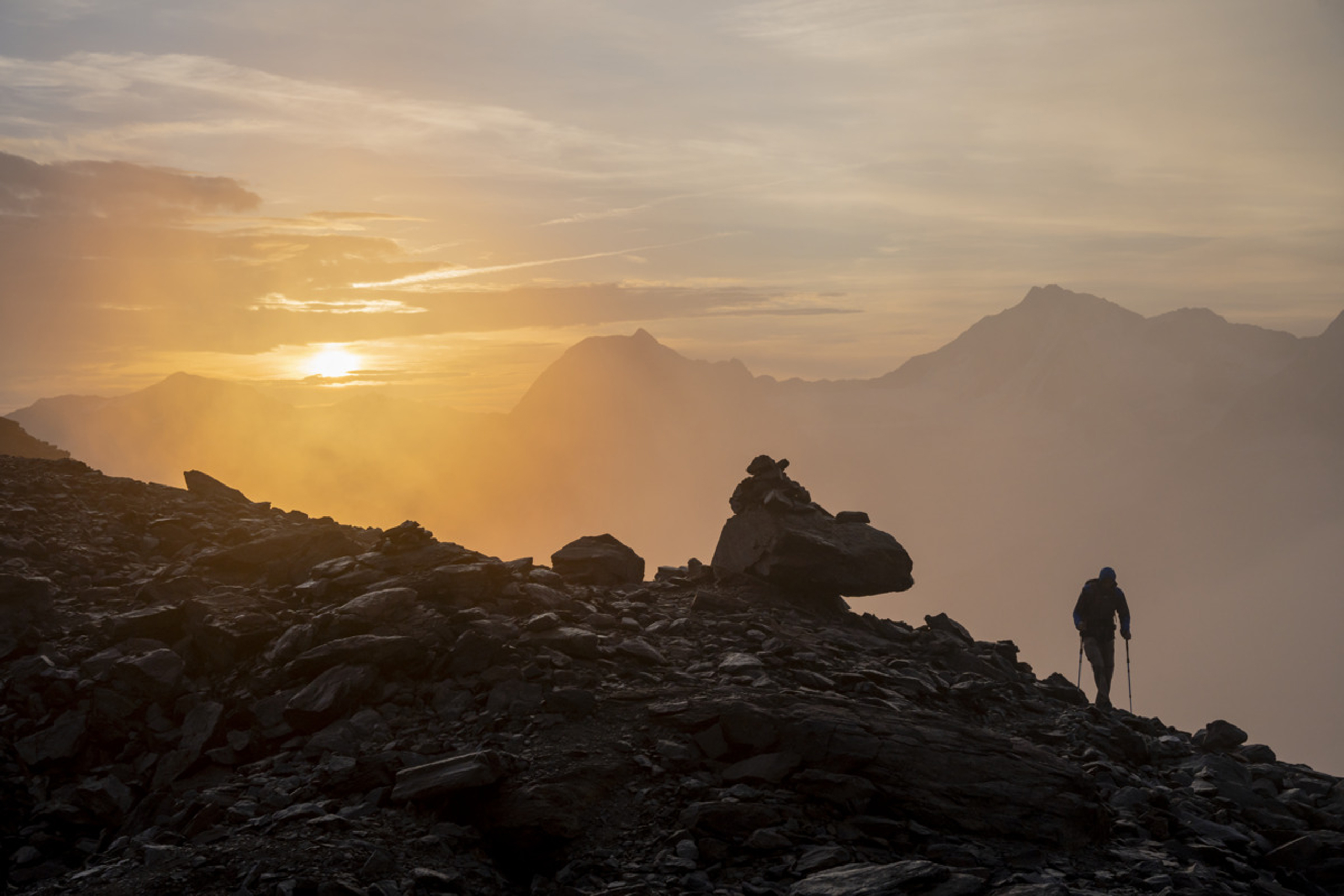 Wanderer auf felsigem Bergpfad bei Sonnenaufgang mit Nebel und Bergen