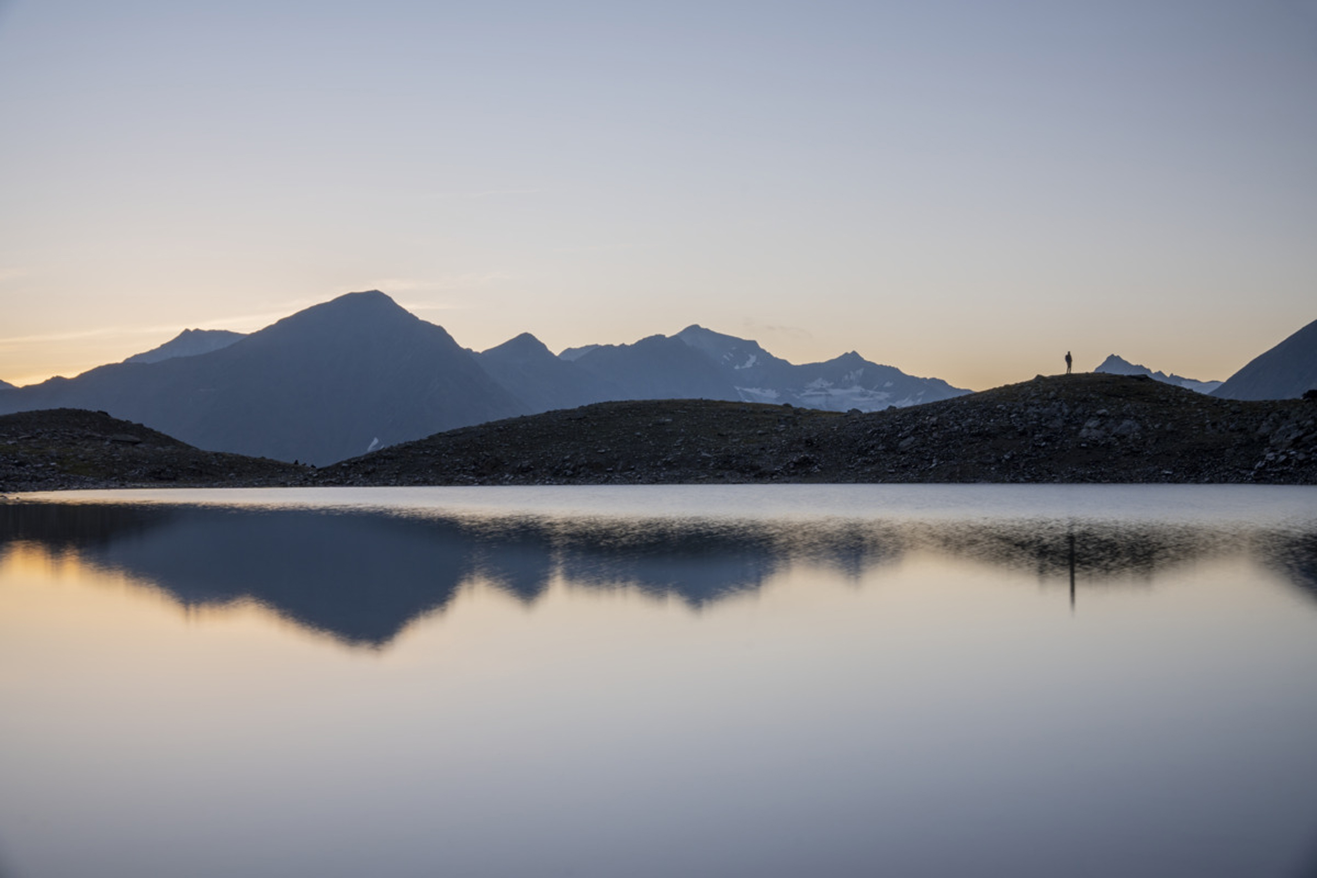 Berglandschaft mit See und Person auf Hügel bei Sonnenuntergang