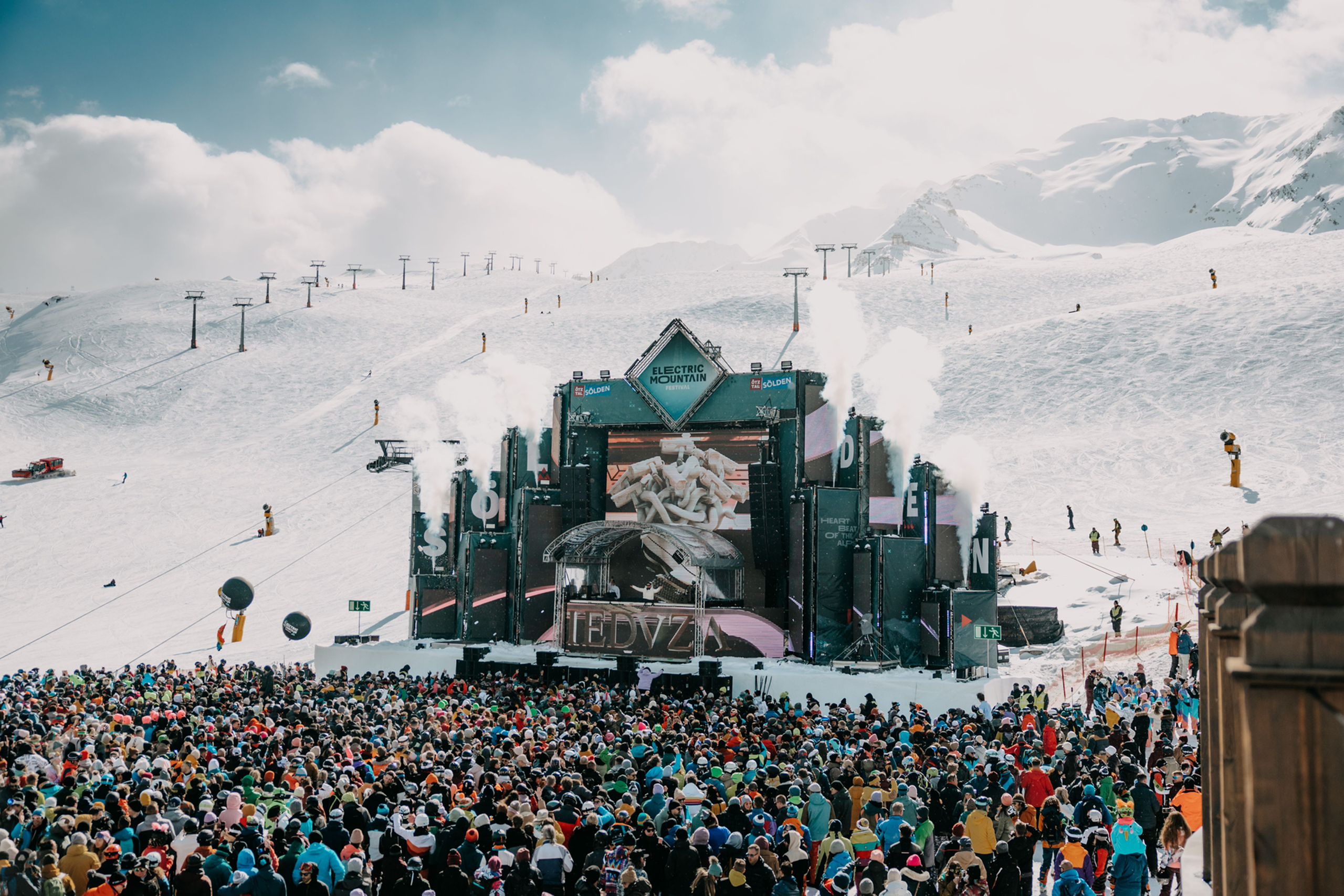 Große Menschenmenge vor Bühne bei Musikfestival in schneebedeckten Bergen