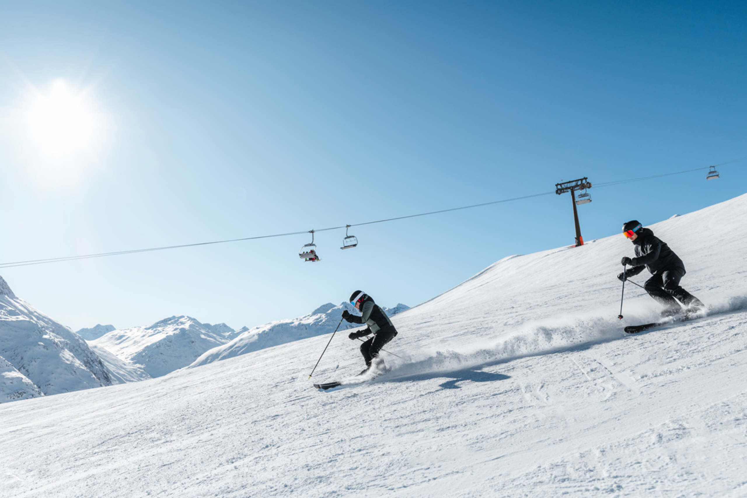 Zwei Skifahrer fahren bei sonnigem Wetter auf schneebedecktem Berghang
