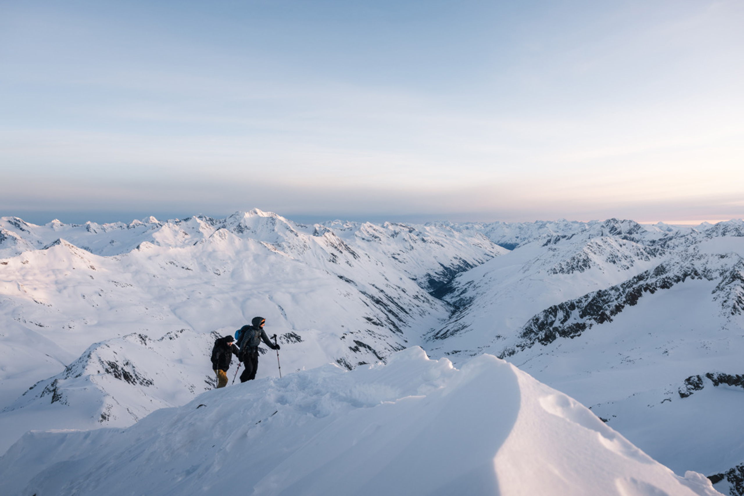 Zwei Wanderer besteigen schneebedeckten Berg mit Alpenpanorama bei Sonnenuntergang