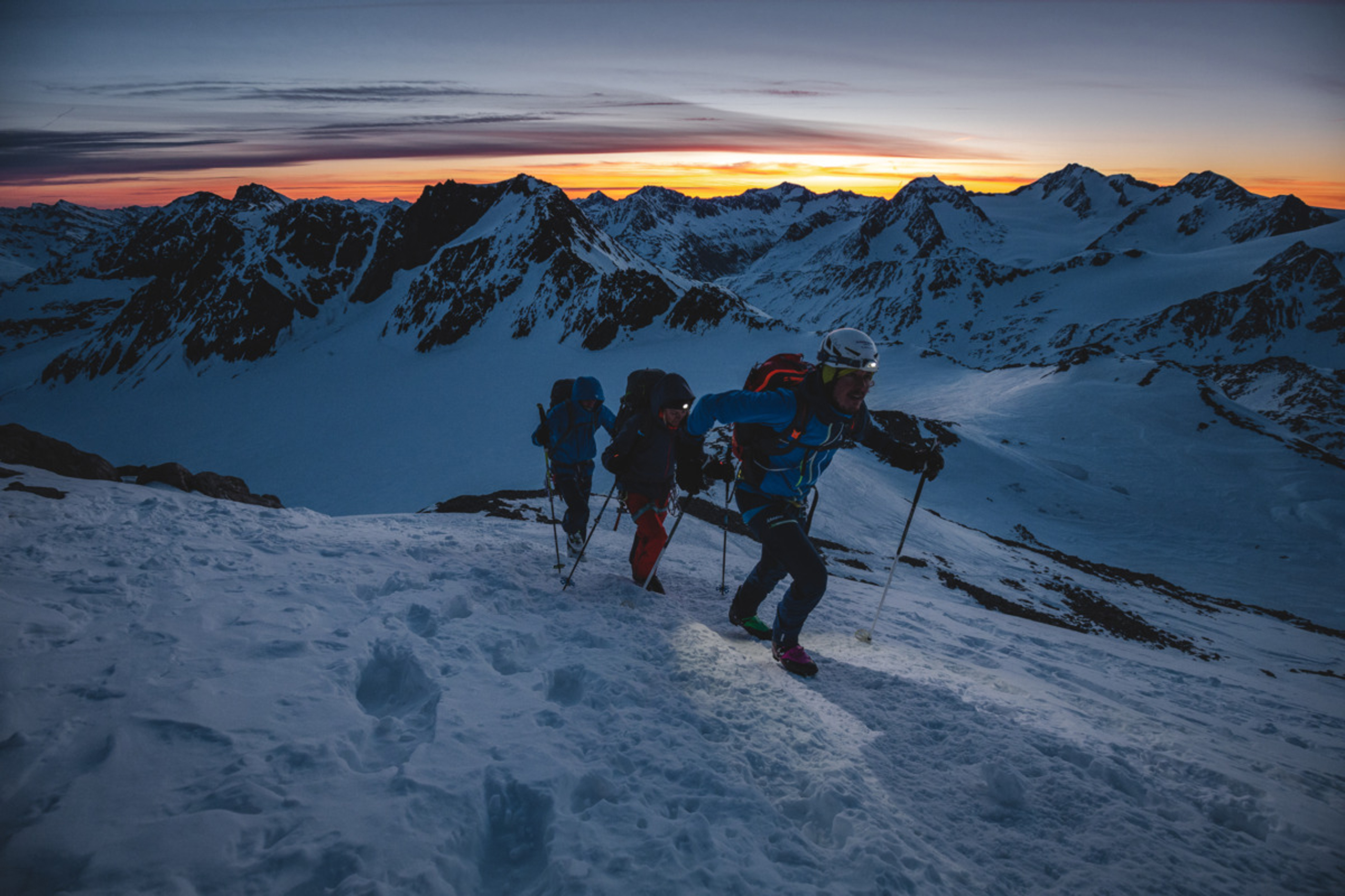 Drei Bergsteiger steigen bei Sonnenaufgang durch verschneite Berge