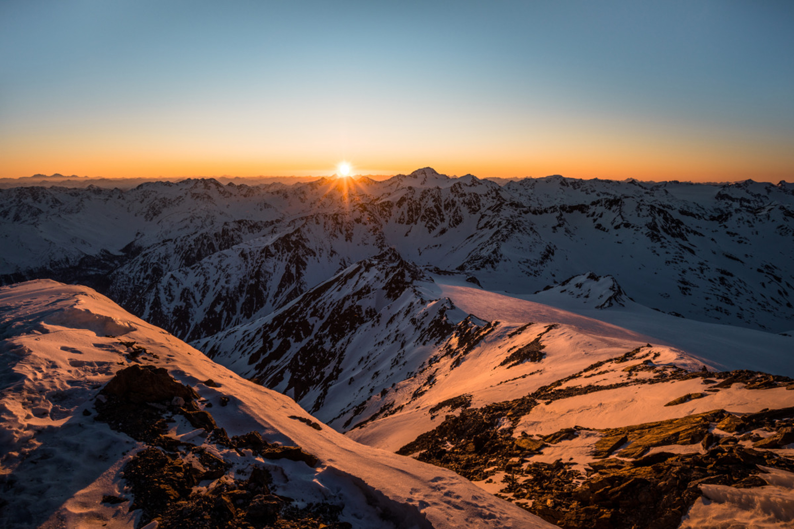 Sonnenaufgang über schneebedeckten Bergen mit orangefarbenem Himmel