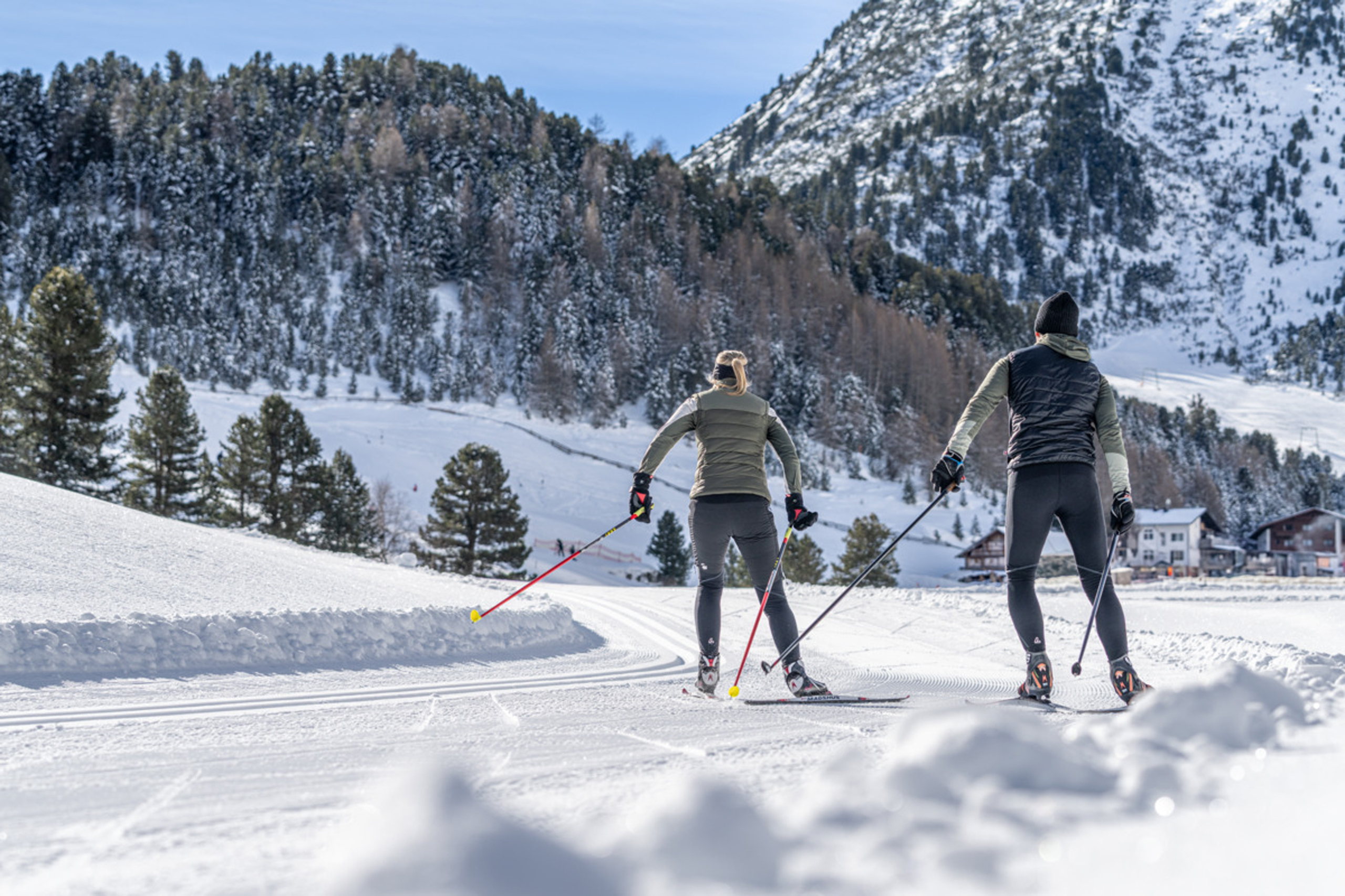 Zwei Personen beim Langlaufen auf verschneiter Loipe vor Bergkulisse